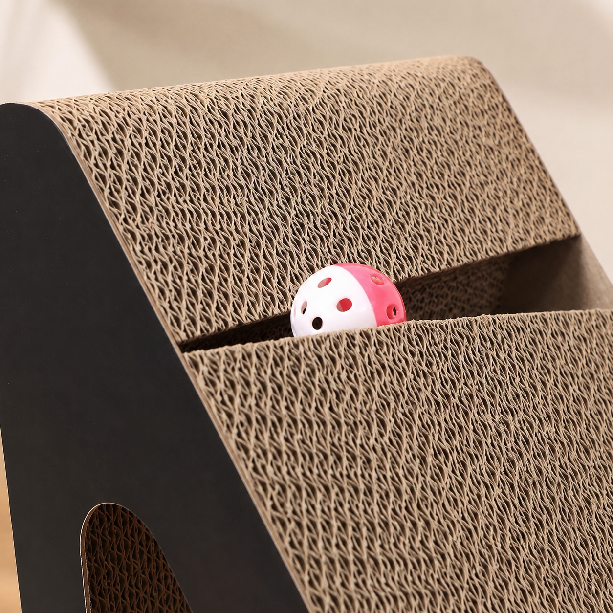 Gros plan du griffoir incliné en carton ondulé avec balle rose intégrée pour stimuler le jeu du chat.
